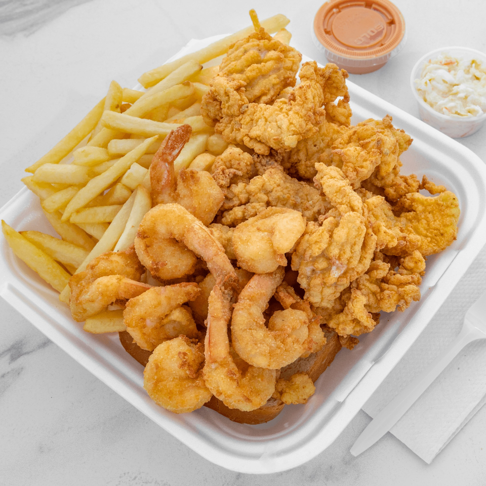 Fried shrimp and clam strips with french fries, coleslaw, and dipping sauce in a take-out container.