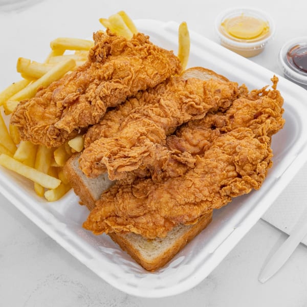 Crispy fried chicken tenders, french fries, and white bread in a takeout container with dipping sauces.
