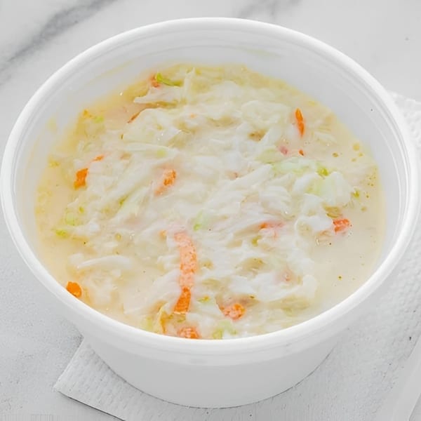 Creamy coleslaw with shredded cabbage and carrots in a white bowl on a white background.