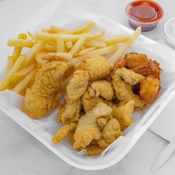 A white tray holds golden fried fish, shrimp, and french fries with dipping sauces.