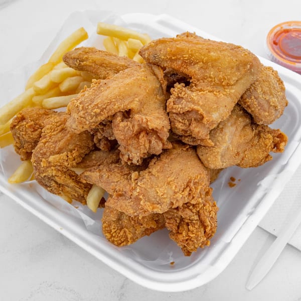 Crispy fried chicken wings and golden french fries in a white takeout container with dipping sauce.