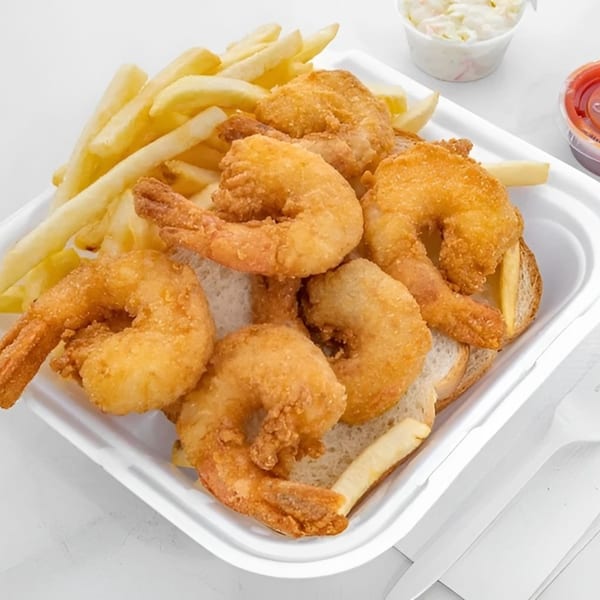 Golden fried shrimp and french fries served in a white takeout container with coleslaw and ketchup.