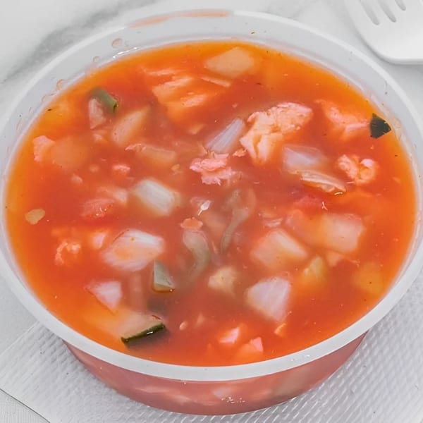 Close-up of a bowl of red soup with chunks of vegetables and meat, with a white fork nearby.