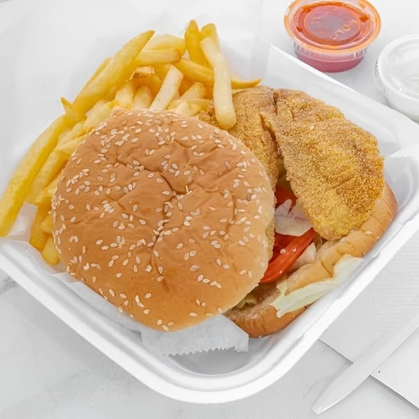Fried fish sandwich with lettuce, tomato, and onions, served with a side of french fries.