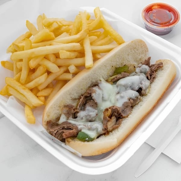 Cheesesteak sandwich with melted cheese, green peppers, and onions, served with a side of fries.