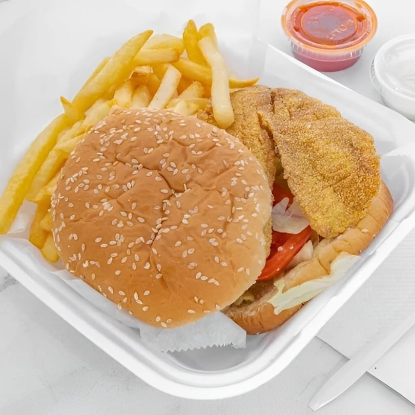 Fried fish sandwich with lettuce, tomato, and onions, served with a side of french fries.