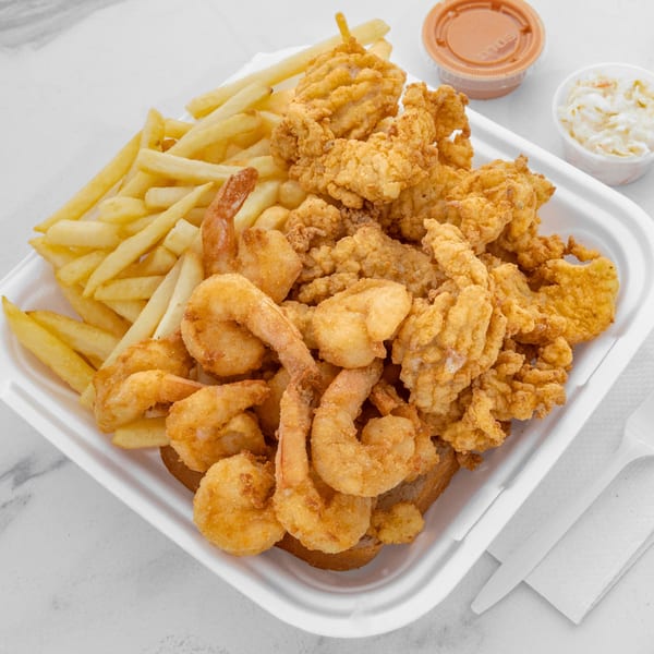 Fried shrimp and clam strips with french fries, coleslaw, and dipping sauce in a takeout container.